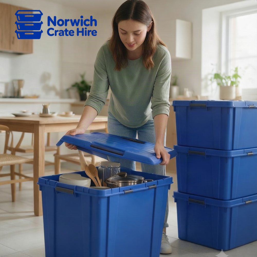 Woman packing kitchenware — pans, bowls and wooden utensils — into a blue Norwich Crate Hire moving crate